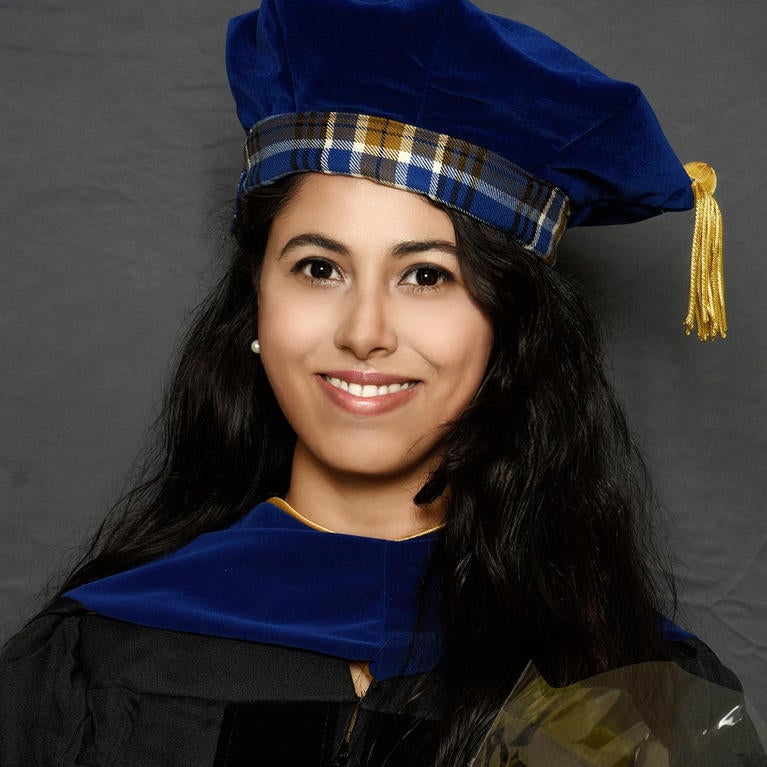 Graduation picture of Antara from the shoulders up, wearing tartan tam and holding flowers