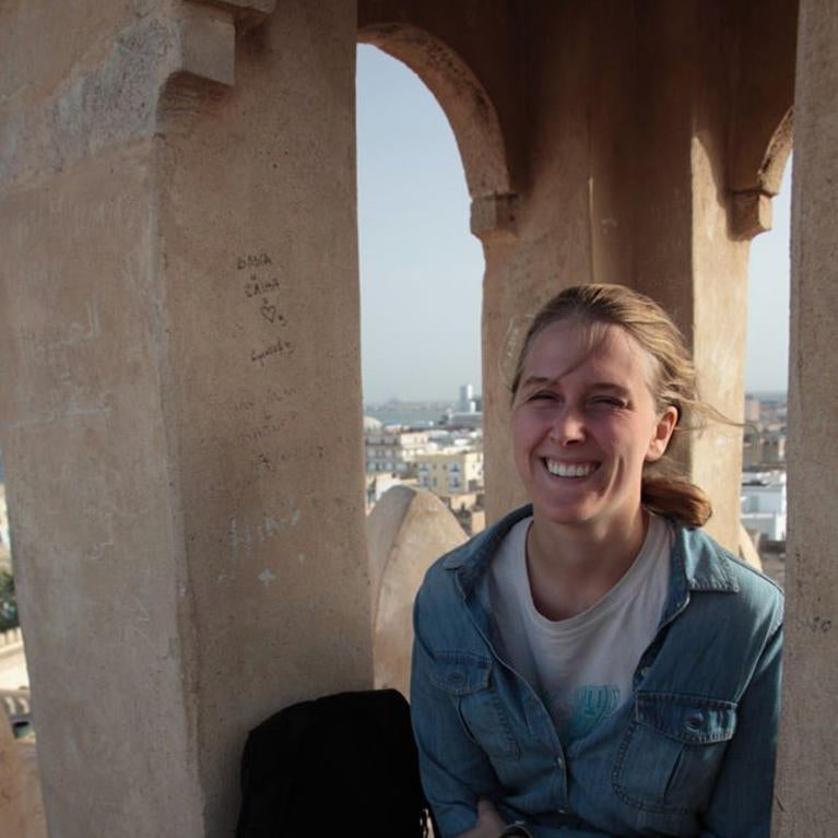 Jessic sits in an arch at the top of a building, with Marrakesh in the background