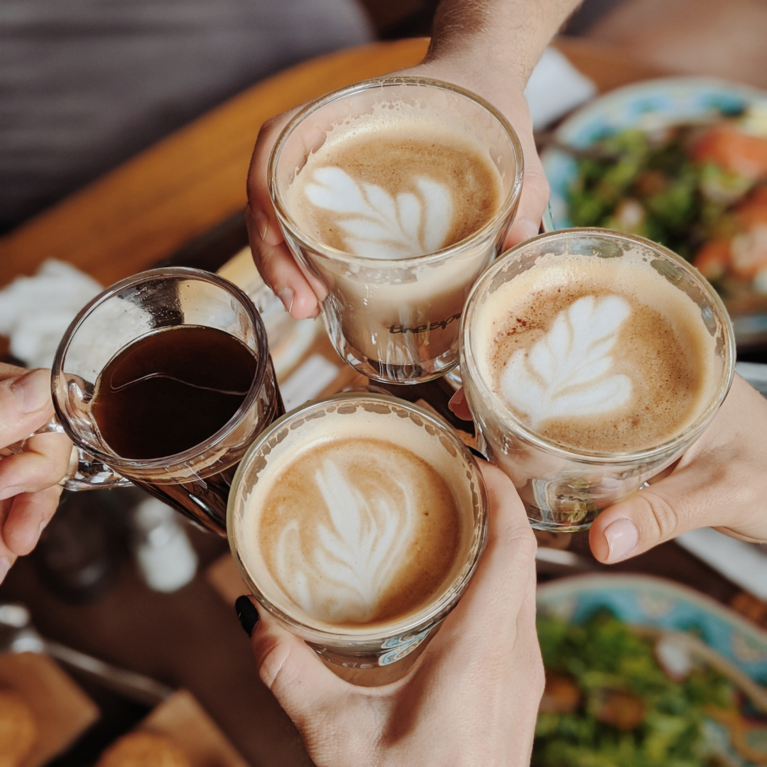 Four hands come together to toast with their coffee cups.