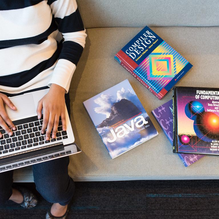 Student sitting on couch with coding books beside her.
