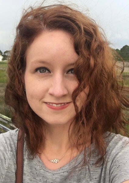 Headshot of Alexis smiling at the camera, her hair in her eyes