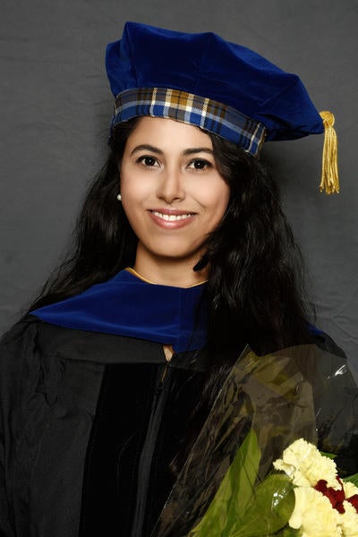 Graduation picture of Antara from the shoulders up, wearing tartan tam and holding flowers