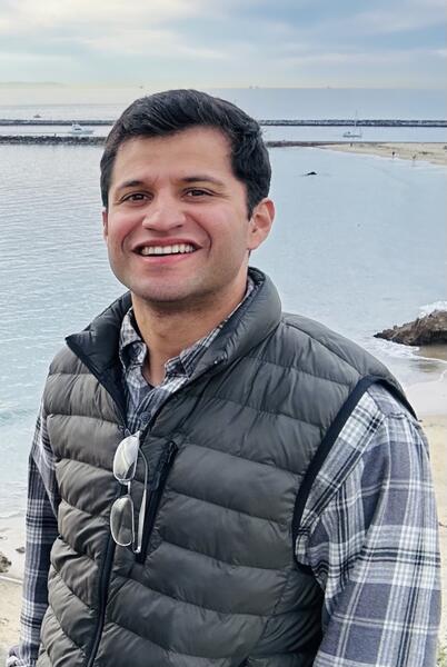 Chris in a puffer vest standing in front of body of water, smiling. 