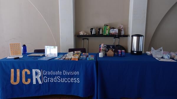 A blue clothed table with snacks and coffee cans on top.