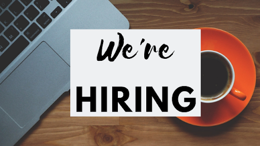 Text reads "We're Hiring" over an aerial view of a desk with a laptop and coffee