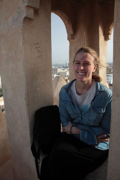 Jessic sits in an arch at the top of a building, with Marrakesh in the background