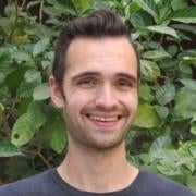 Headshot of Matt smiling in front of a wall of green plants