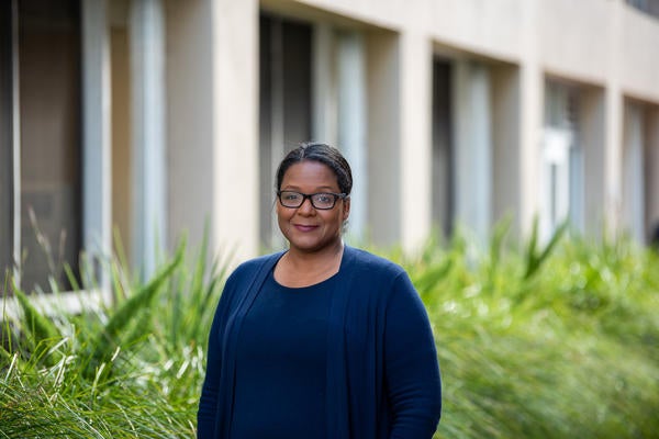 Naledi Saul outside of a building with plants behind her, smiling to the camera