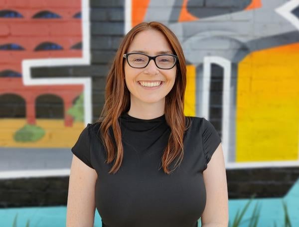 Kyla in a black dress, seen from the waist up, smiling at the camera in front of a colorful backdrop