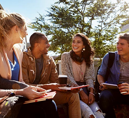 Group of students sitting in sun and chatting with two holding coffee cups