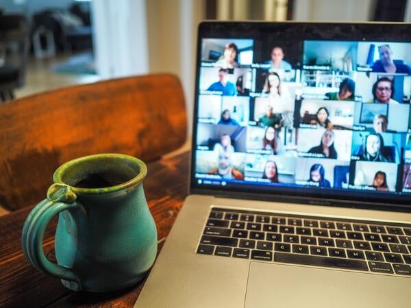 A Zoom conversation is happening on a laptop next to a coffee mug.