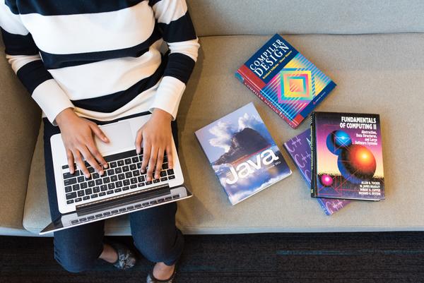 Student sitting on couch with coding books beside her.