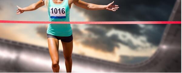 A runner with arms spread out and just about to break the ribbon while crossing a finish line
