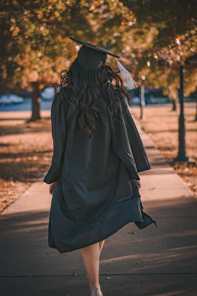 A woman is walking along a pathway while dressed in a graduation cap and long black robe.