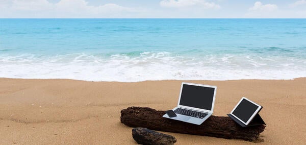 Two gray laptops and a black phone sitting on a log on a beach