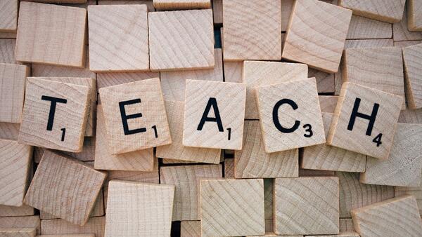 TEACH spelled out in Scrabble tiles over blank tiles