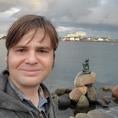 Bryan from the shoulders up, standing in front of the Hans Christian Anderson mermaid statue in Copenhagen harbor.