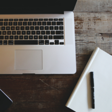 A laptop, a notebook, and a pen on a desk. 